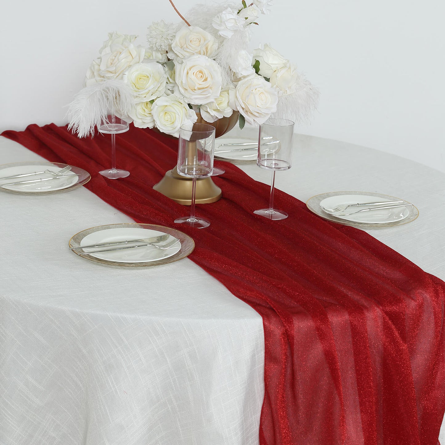 Red sparkling glitter table runner on a white table with floral centerpiece.