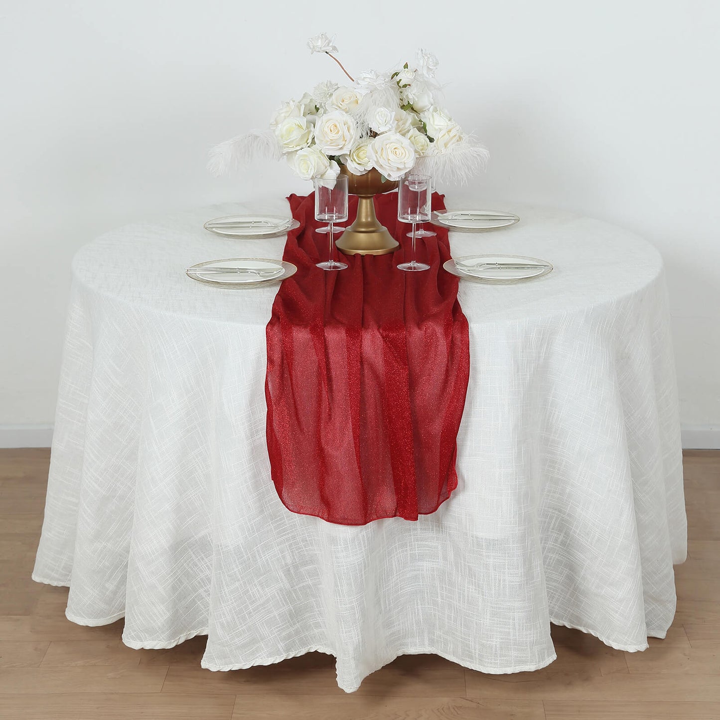 Red sparkling glitter gauze table runner on a white table with floral centerpiece.
