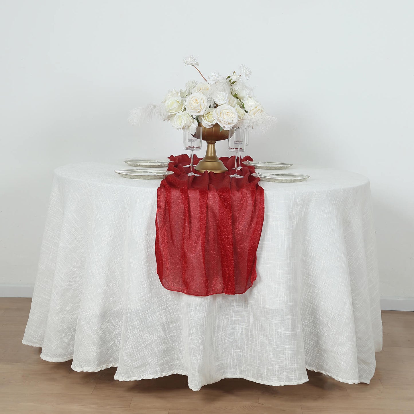 Red sparkling glitter table runner on a white table, adorned with flowers.