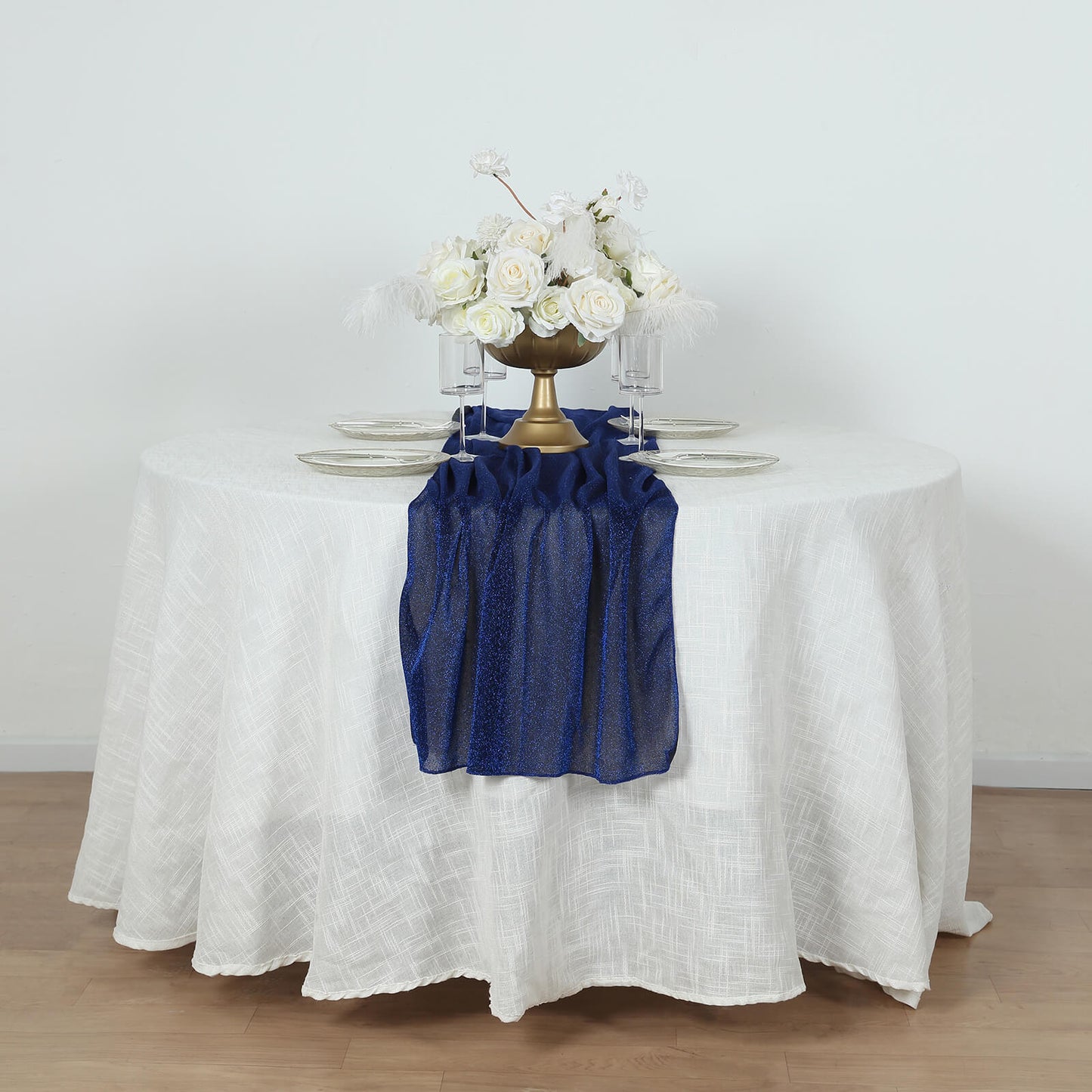 Royal blue glitter gauze table runner on a round white table with floral arrangement.