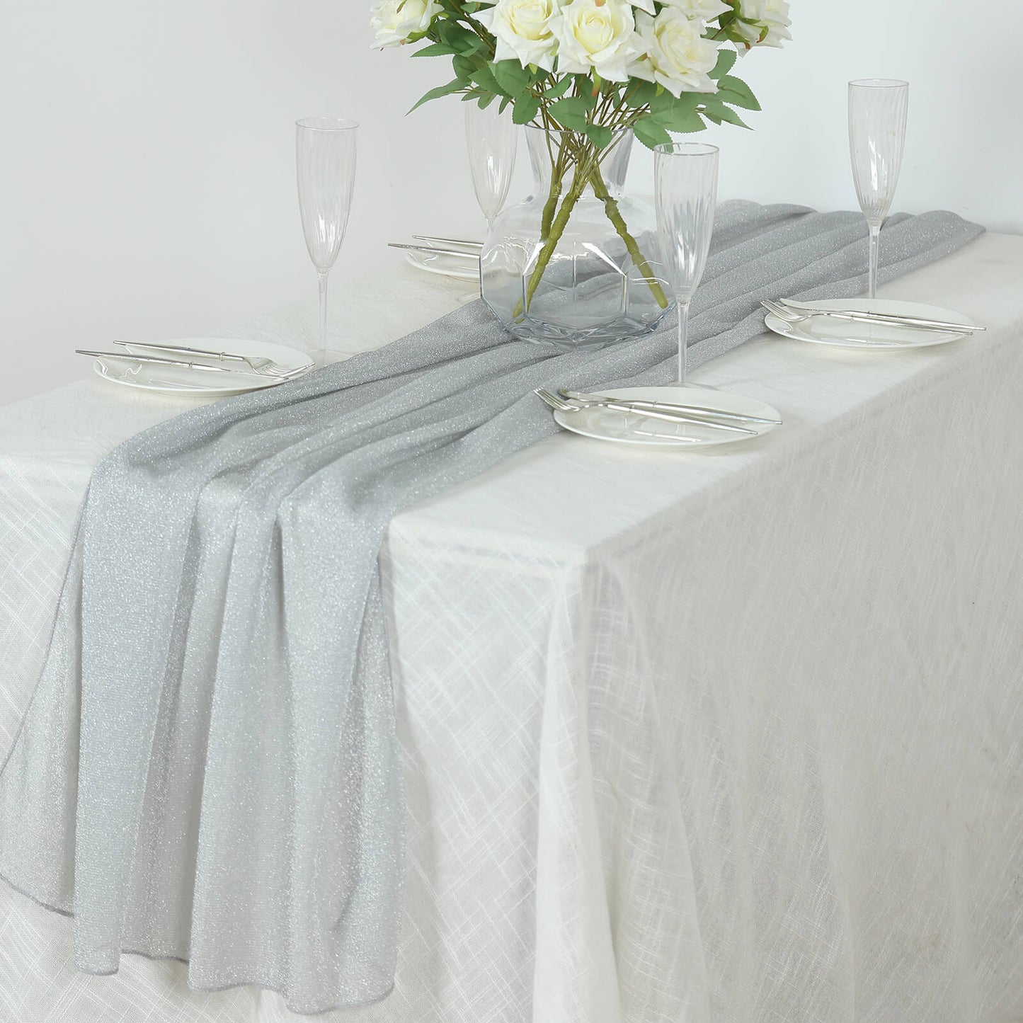Silver sparkling glitter gauze table runner on a white table setting.