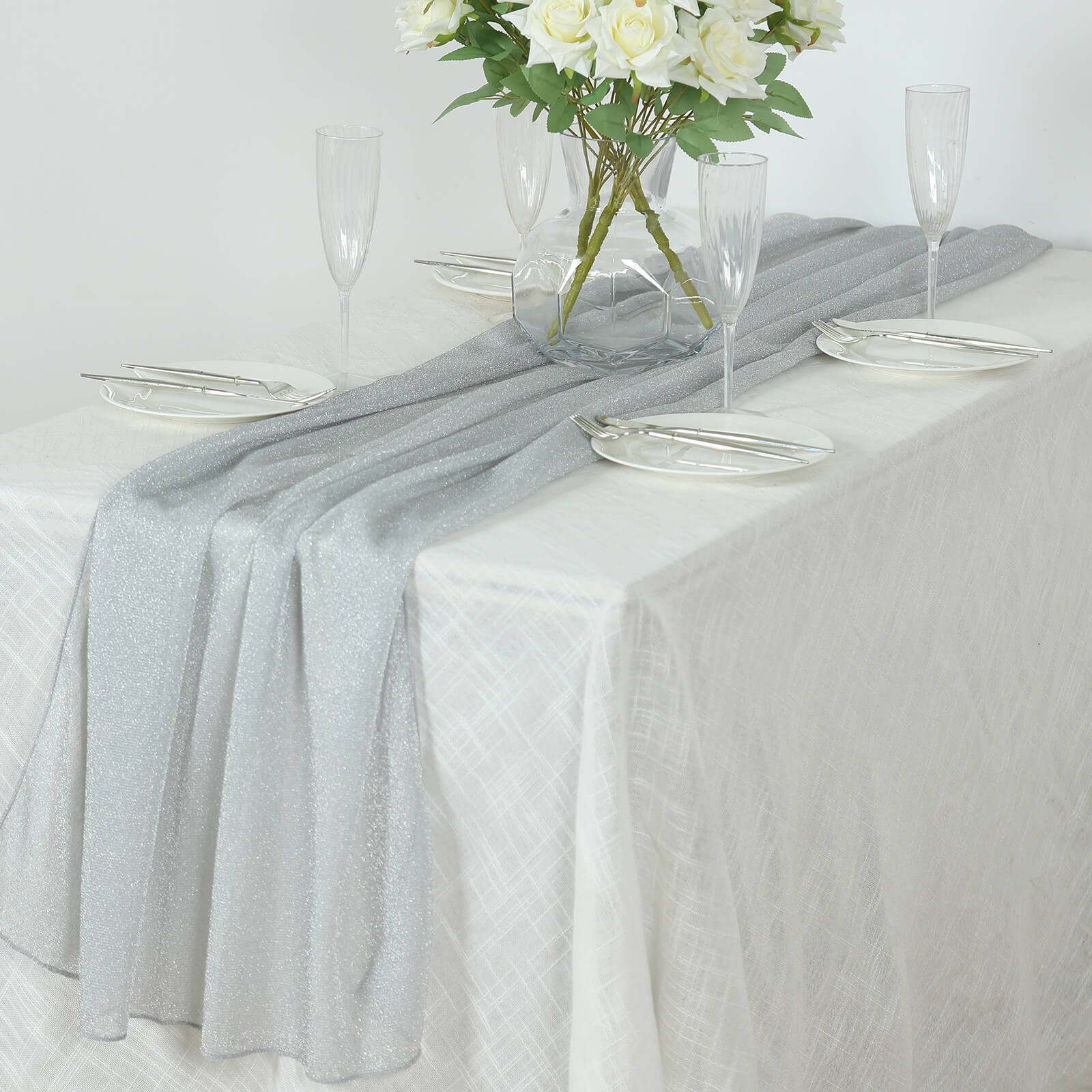 Silver sparkling glitter gauze table runner on a white table setting.