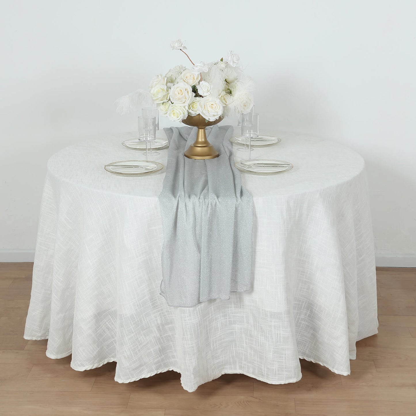 Silver glitter table runner on a round white table with floral centerpiece.