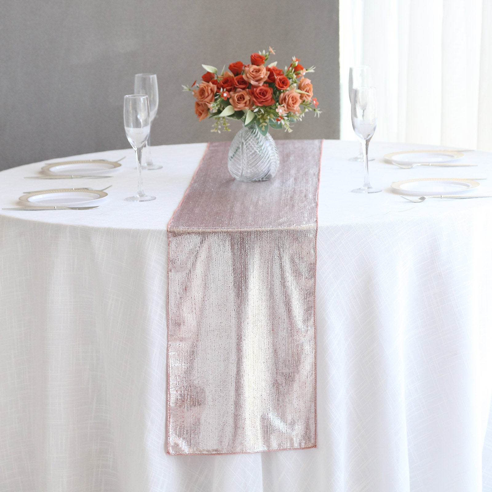Rose gold shimmer sequin table runner on a white table with floral centerpiece.
