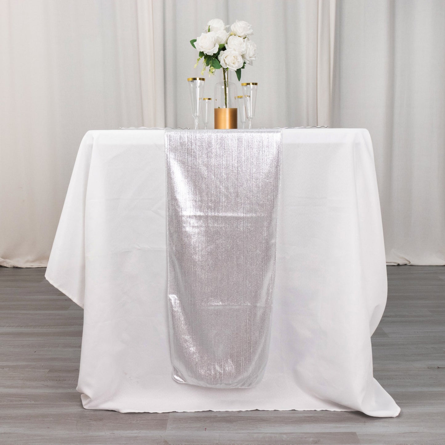 Silver shimmer sequin table runner on a white table with flowers.