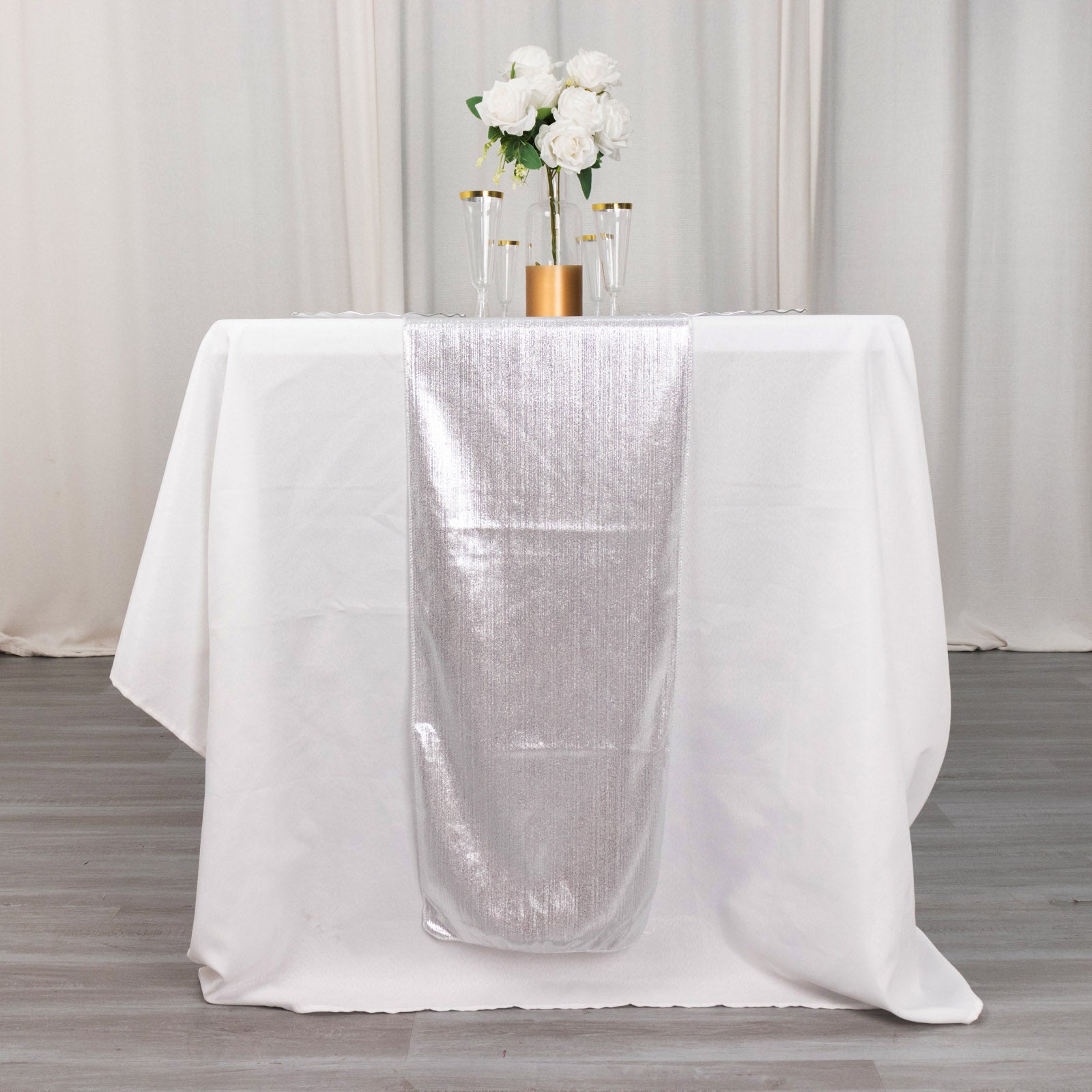 Silver shimmer sequin table runner on a white table with flowers.