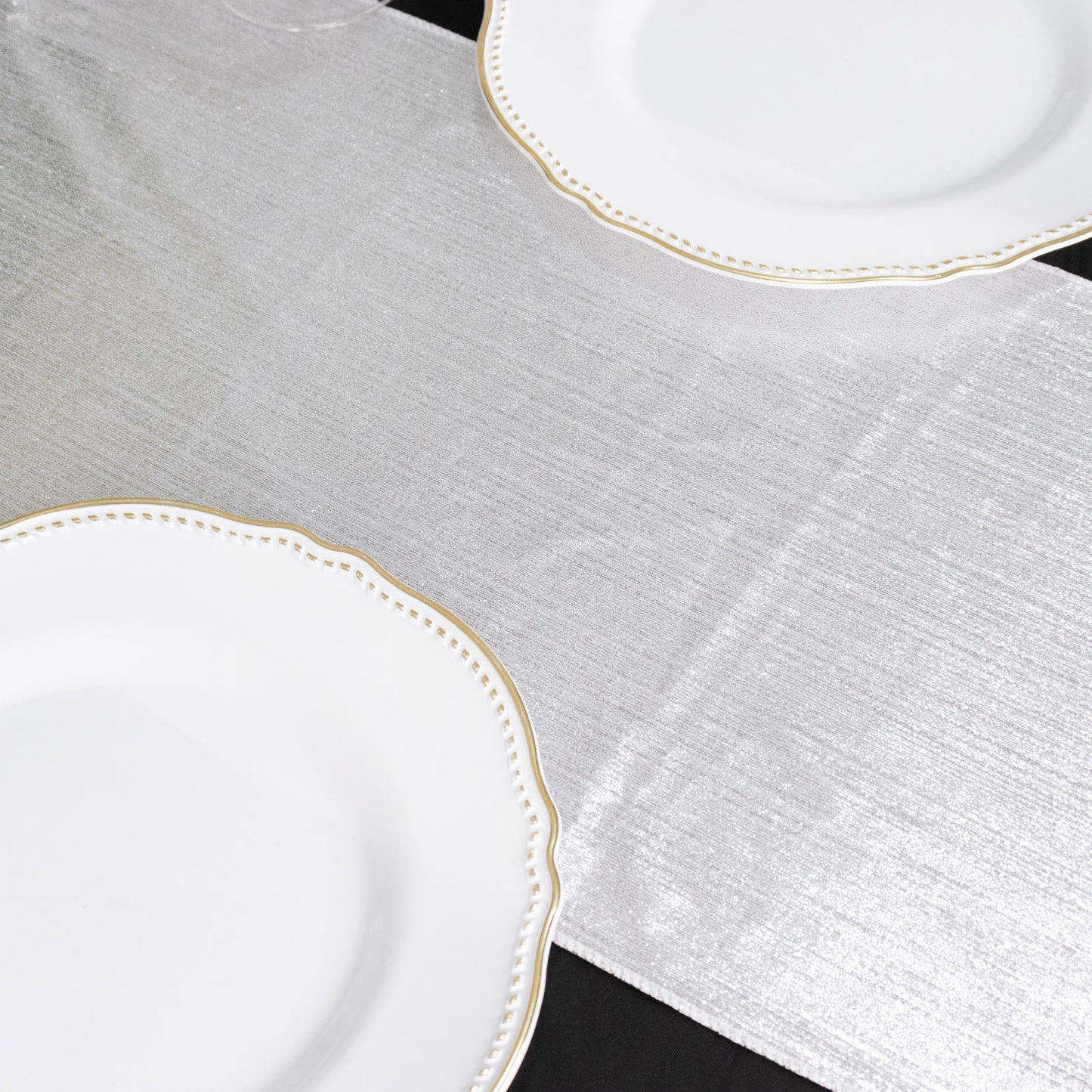 Silver shimmer sequin table runner on a black table with white plates.