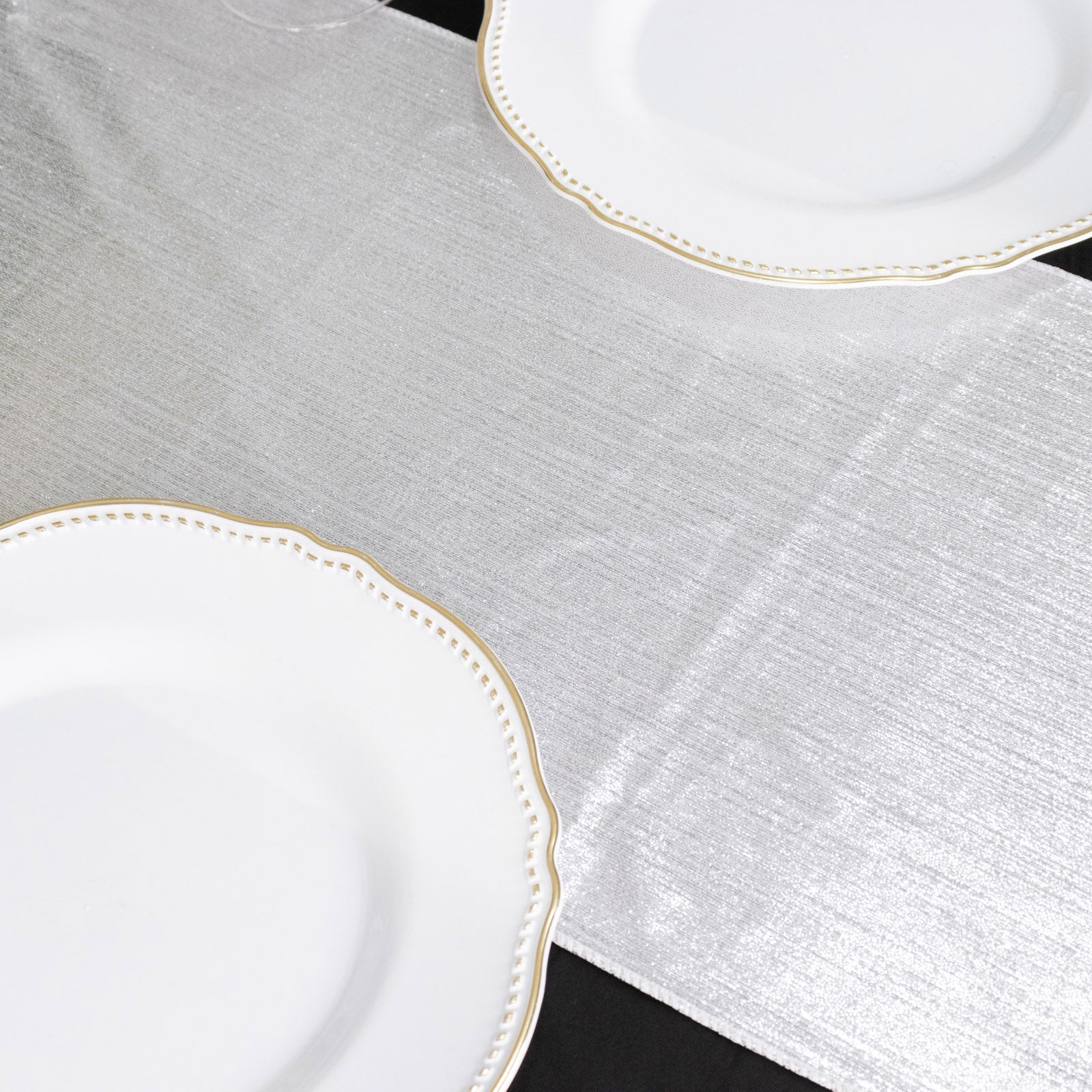 Silver shimmer sequin table runner on a black table with white plates.