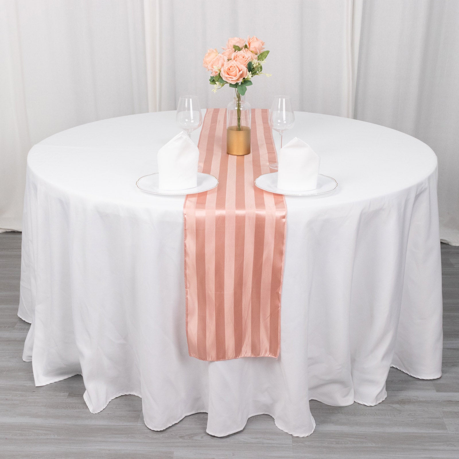 Dusty rose satin stripe table runner on a round table with floral centerpiece.