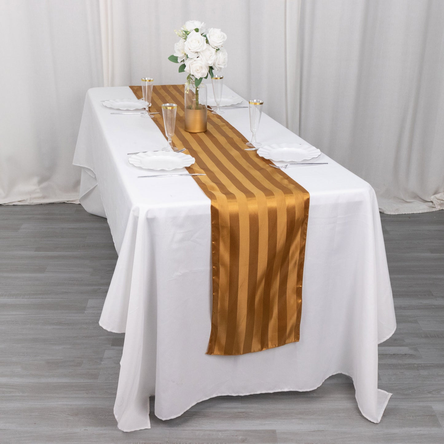 Gold satin stripe table runner on a white table, elegantly set for dining.