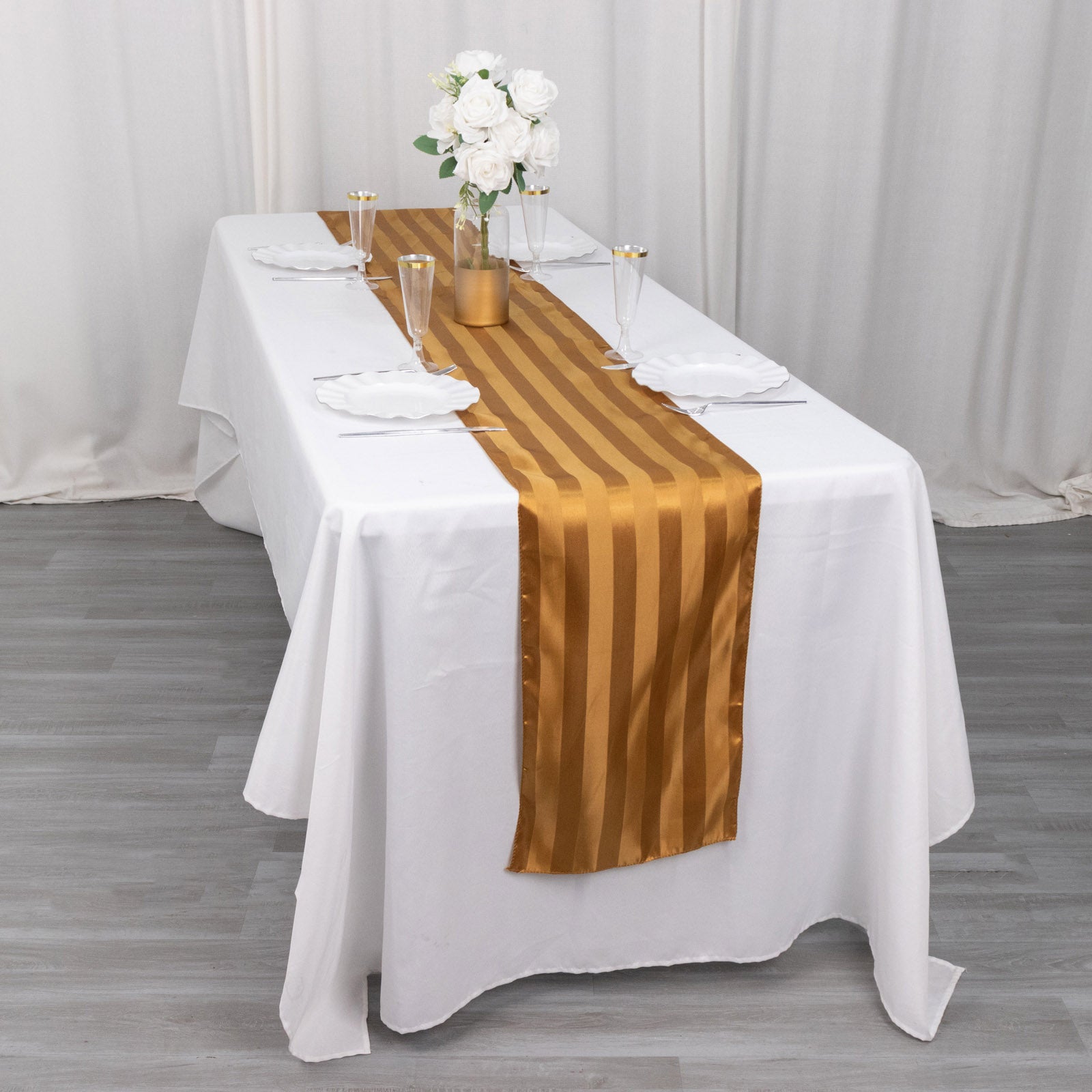 Gold satin stripe table runner on a white table, elegantly set for dining.