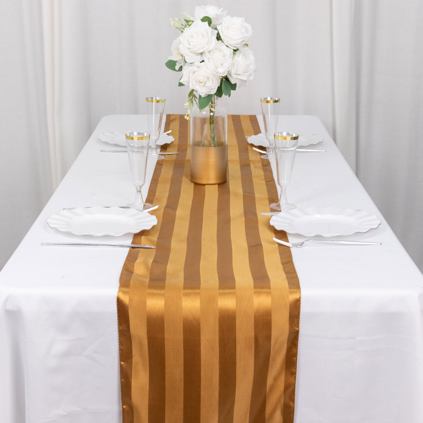 Gold satin stripe table runner on a white table with floral centerpiece.
