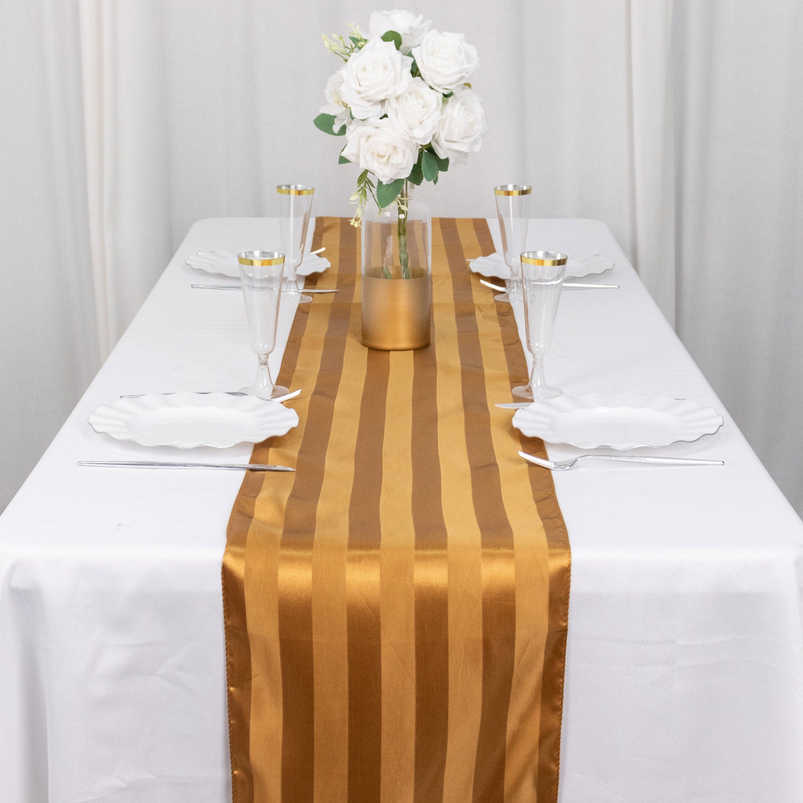 Gold satin stripe table runner on a white table with floral centerpiece.