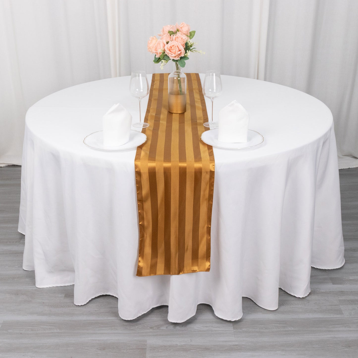 Gold satin stripe table runner on a round table with white tablecloth.