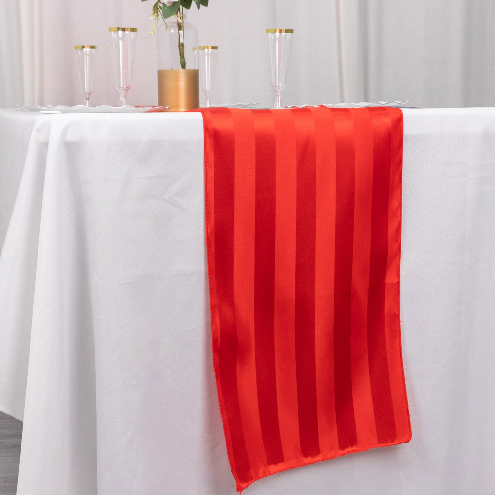 Red satin stripe table runner on a white tablecloth.
