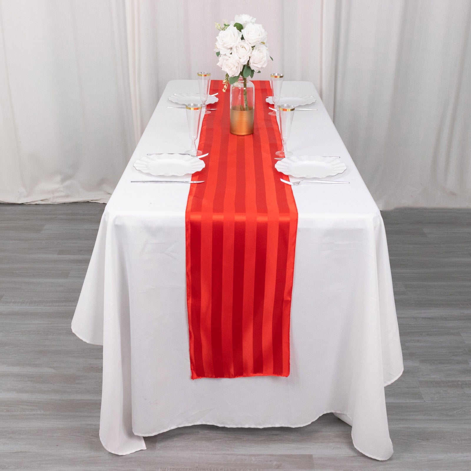 Red satin stripe table runner on a white tablecloth.