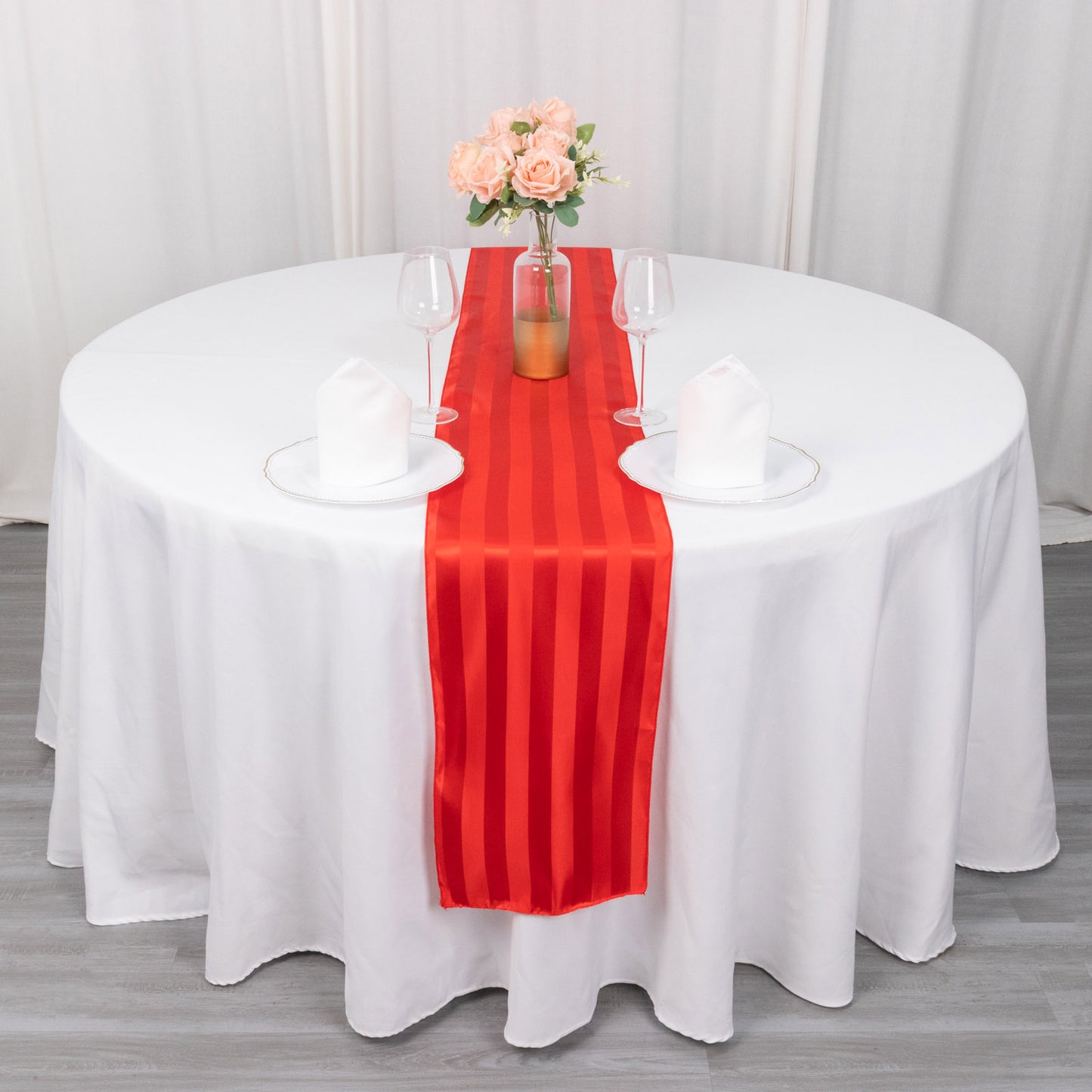 Red satin stripe table runner on a round table with floral centerpiece.