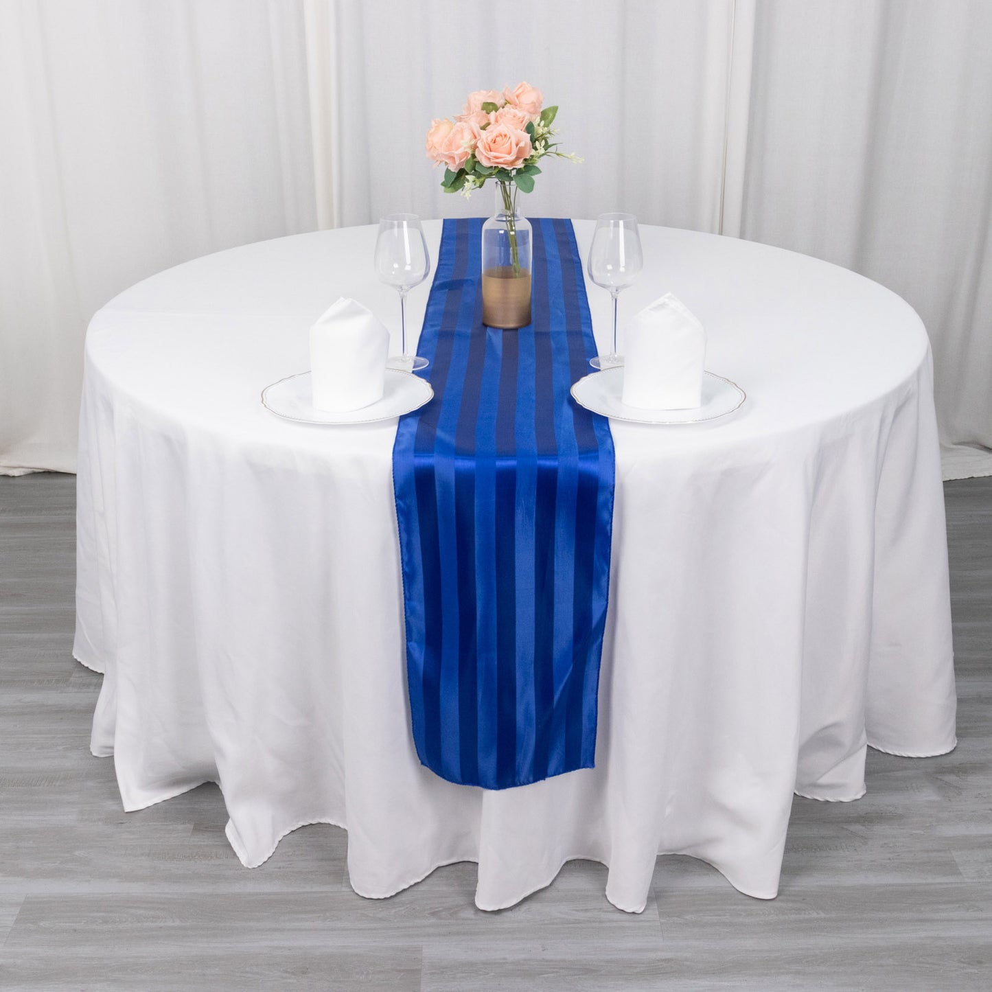 Royal blue satin stripe table runner on a round table with floral centerpiece.