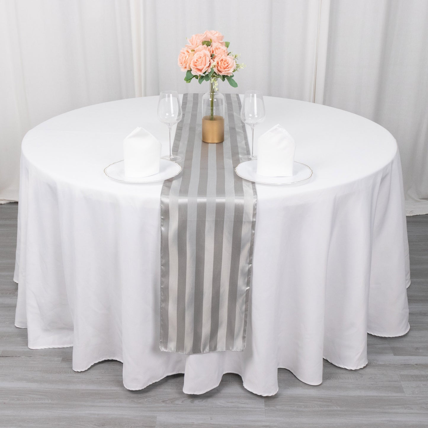 Silver satin stripe table runner on a white table with floral centerpiece.