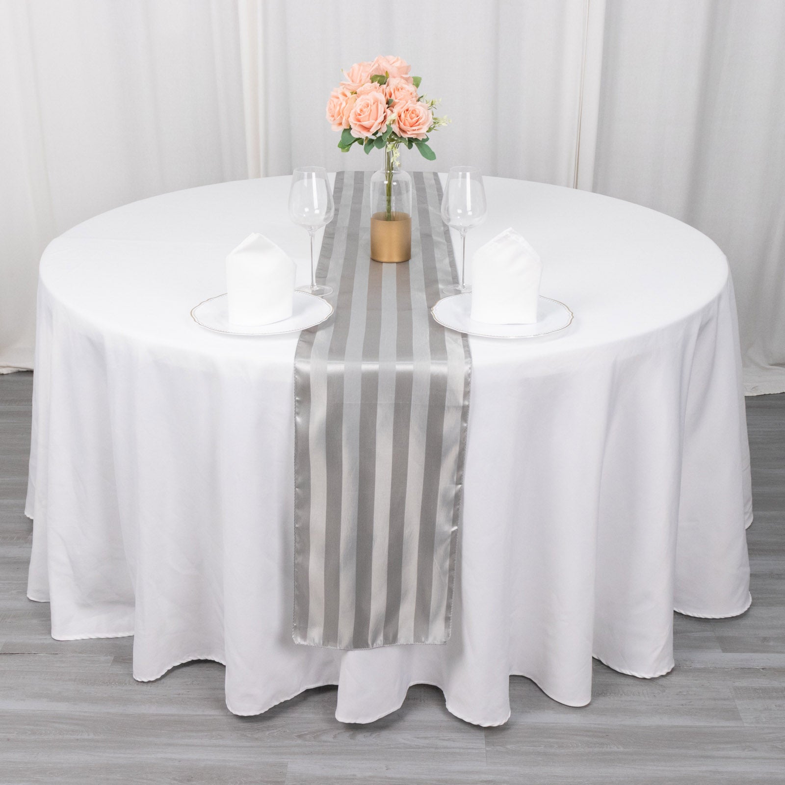 Silver satin stripe table runner on a white table with floral centerpiece.