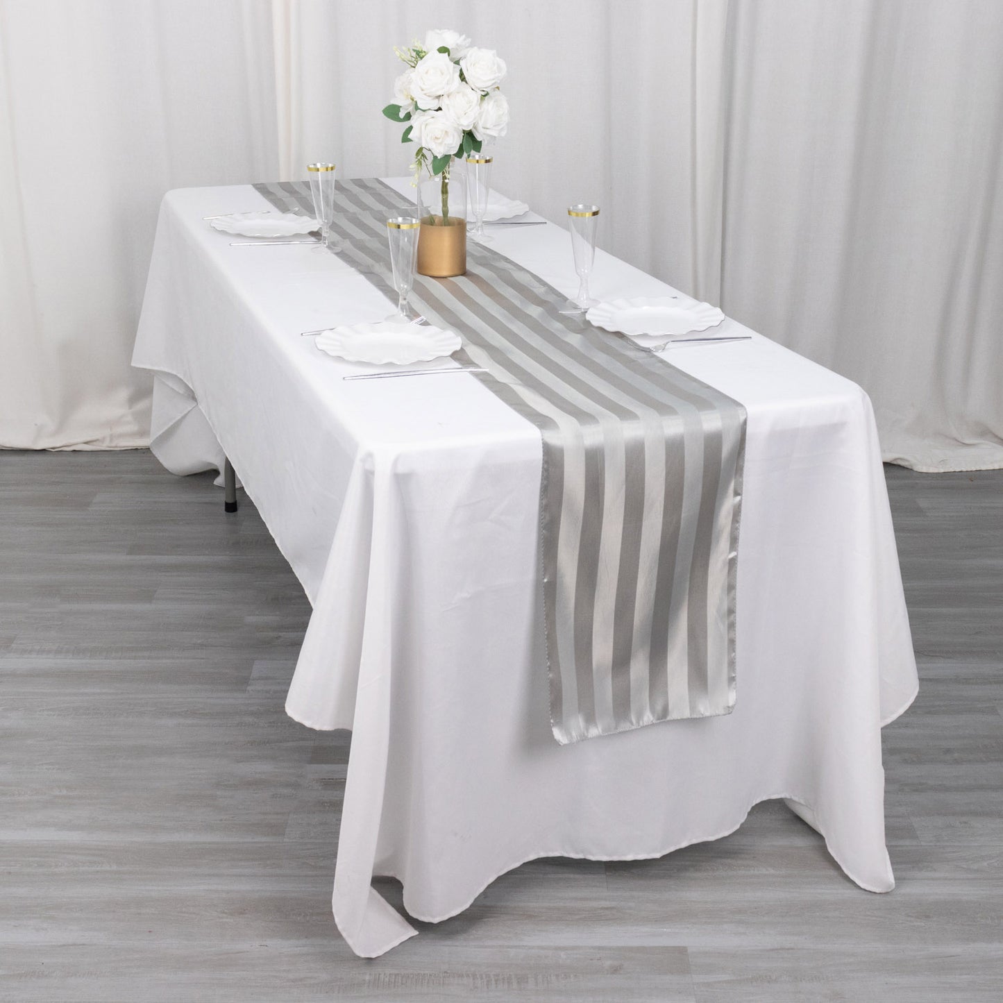 Silver satin stripe table runner on a white table with floral decor.