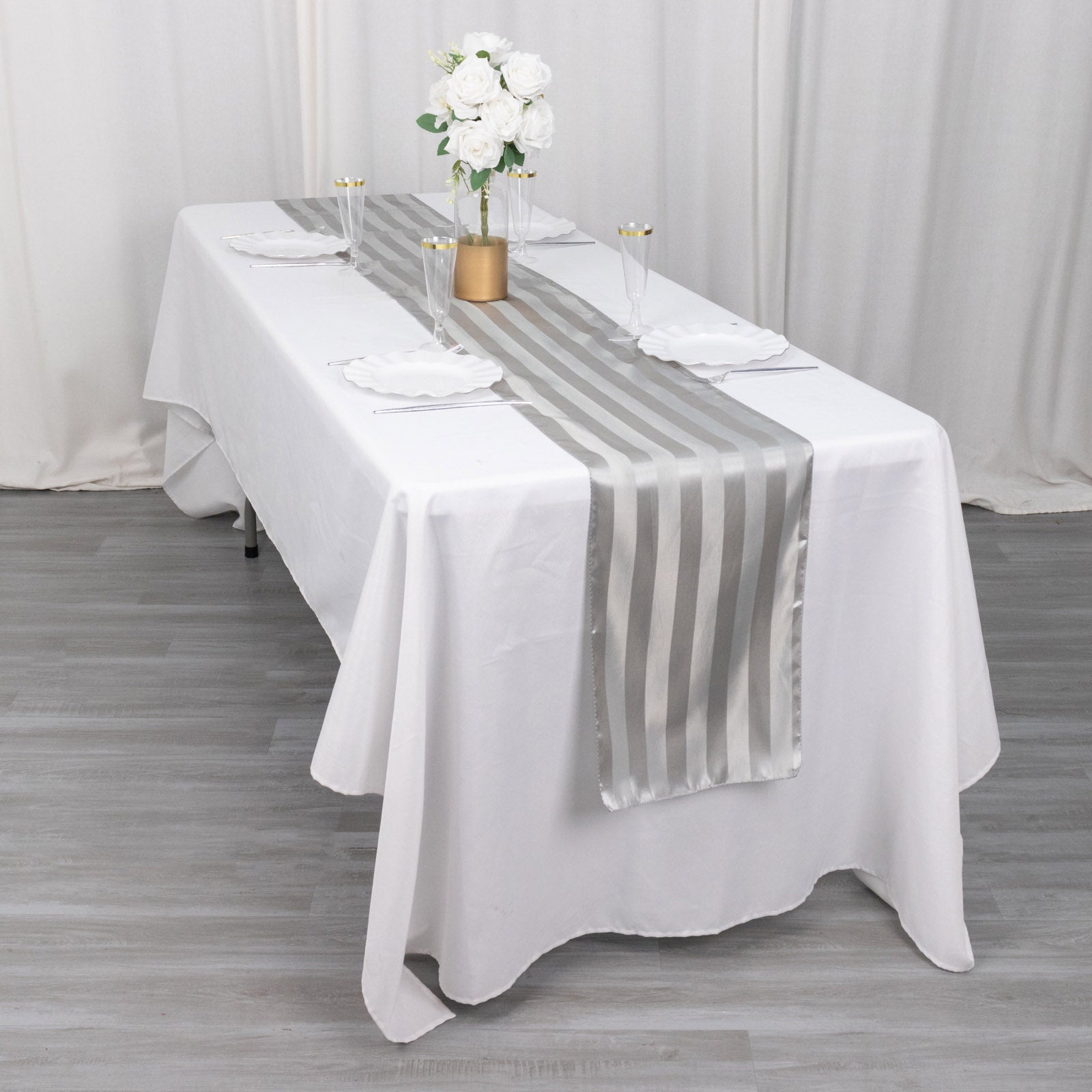 Silver satin stripe table runner on a white table with floral decor.