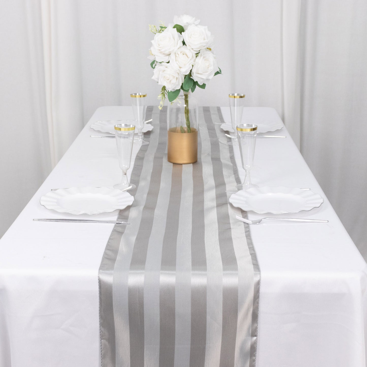 Silver satin stripe table runner on a white tablecloth with floral centerpiece.