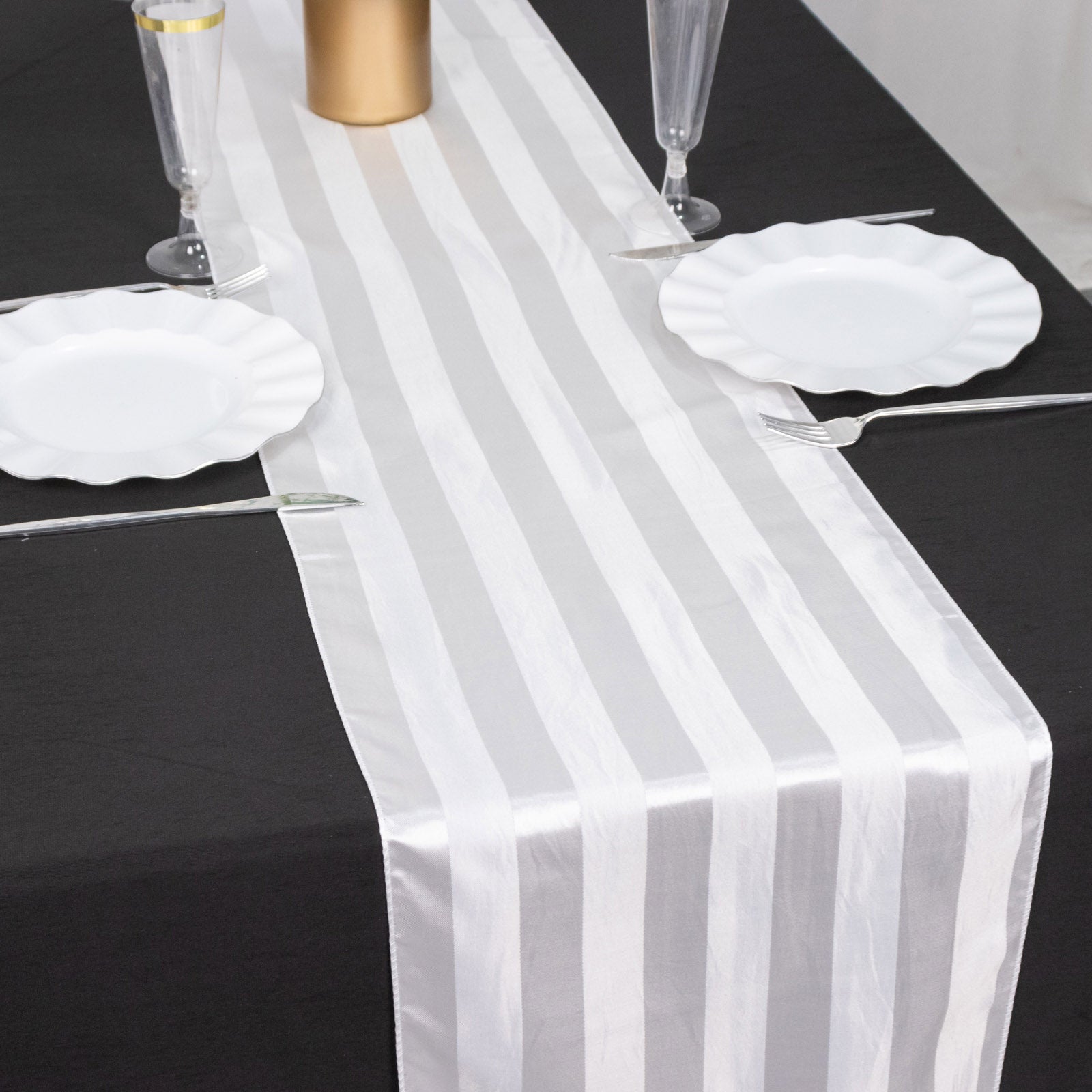 White satin stripe table runner on a black table with elegant dinnerware.