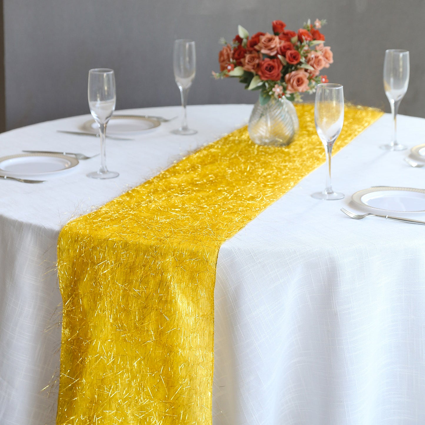 Gold metallic fringe table runner on a white table, surrounded by glassware and flowers.
