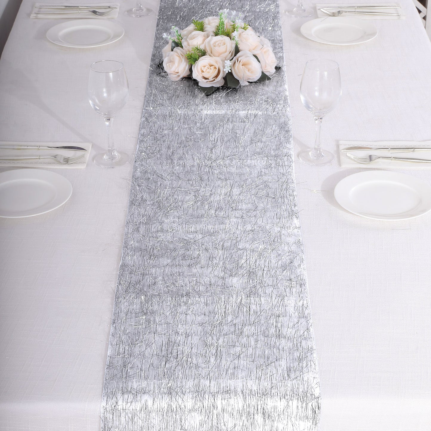 Silver metallic fringe tinsel table runner on a white table with flowers.