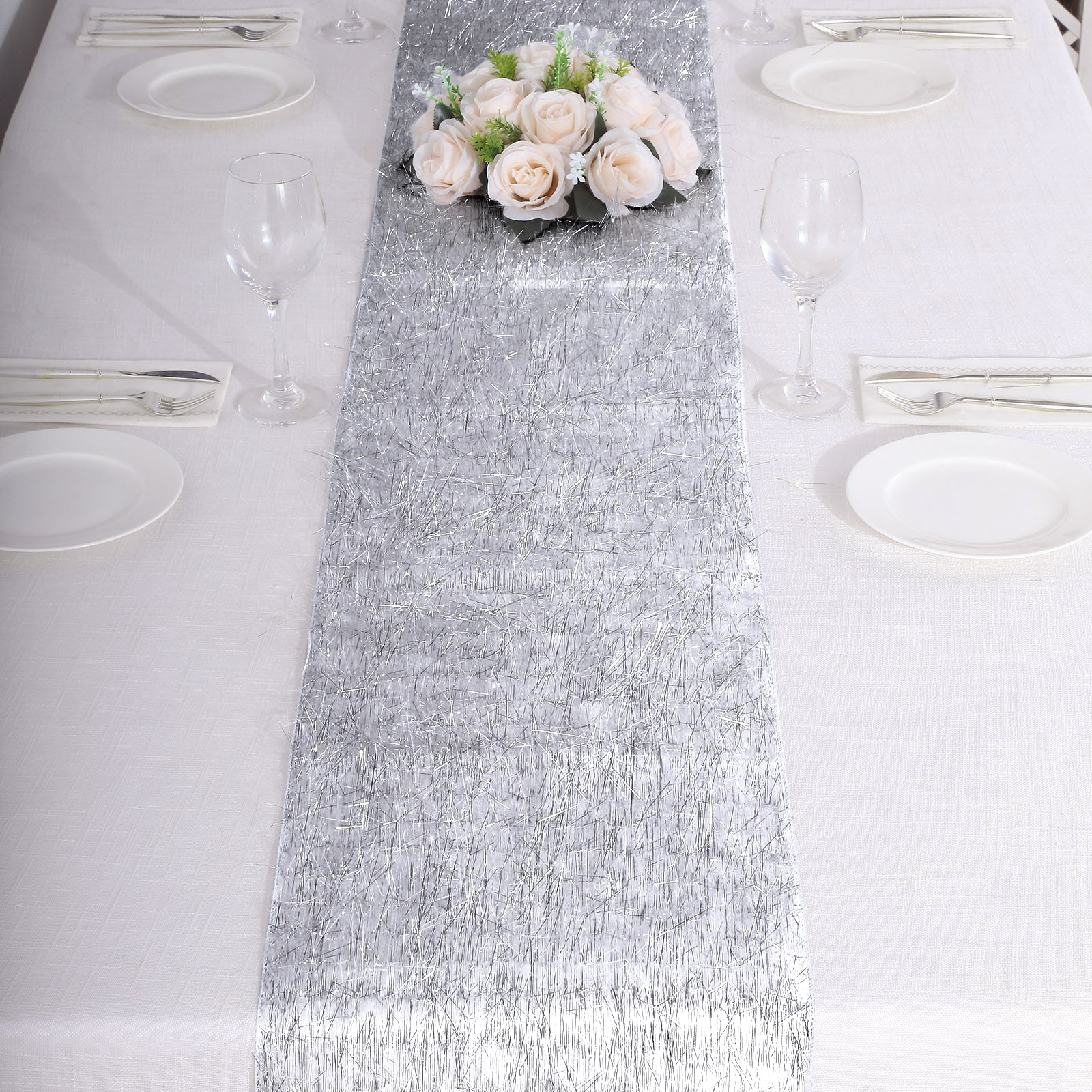 Silver metallic fringe tinsel table runner on a white table with flowers.