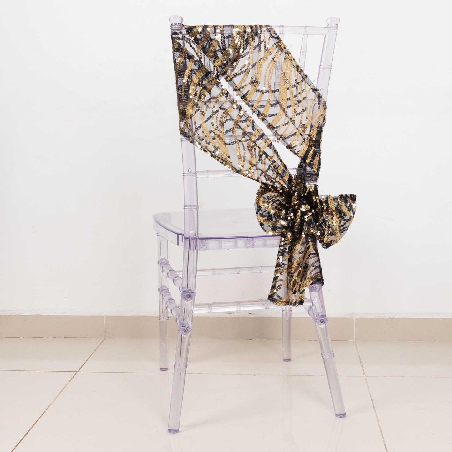 Black and gold wave embroidered sequin chair sash on a clear chair.