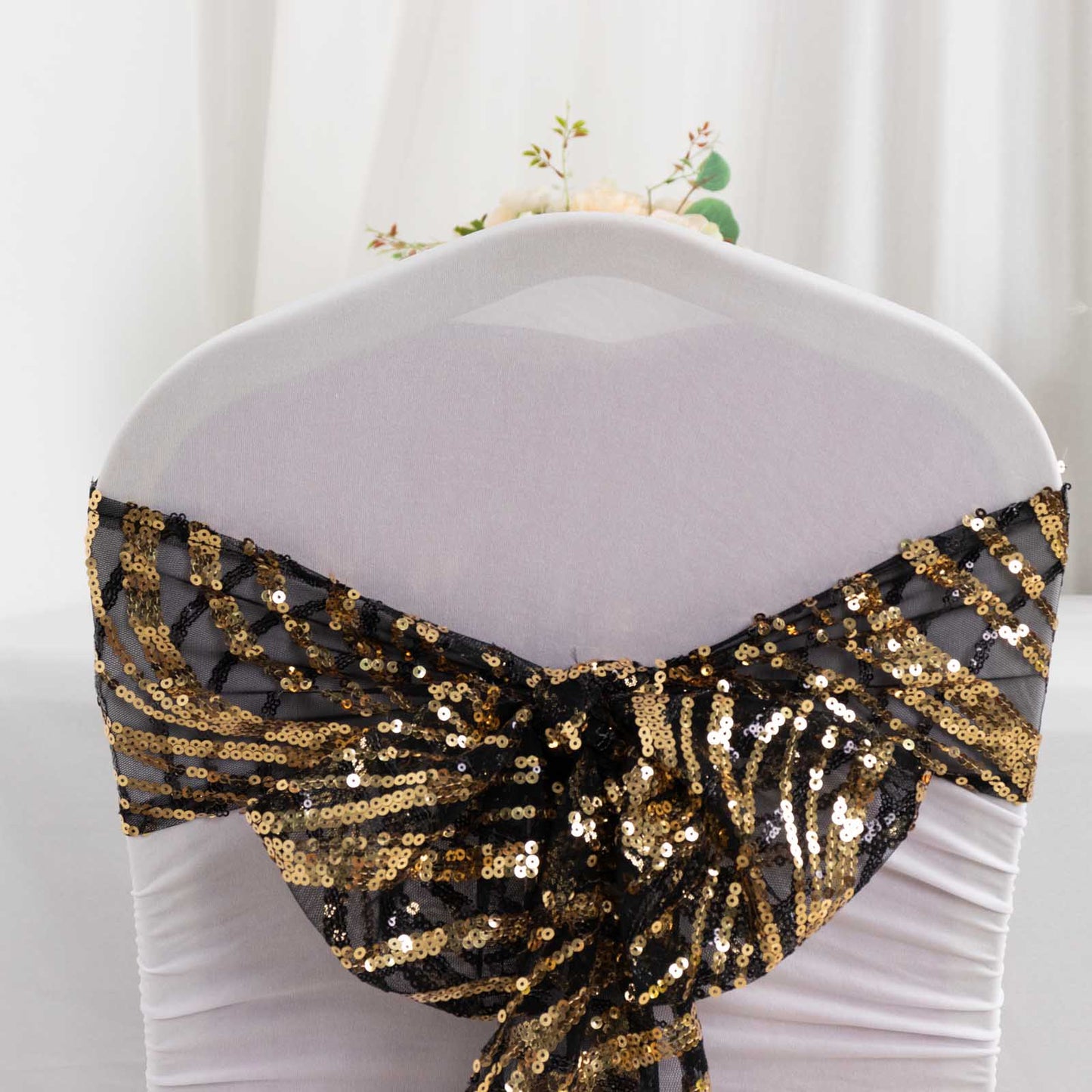 Black and gold wave embroidered sequin chair sash on a white chair.