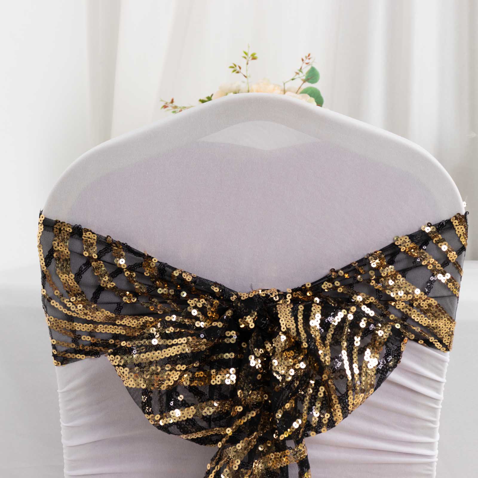 Black and gold wave embroidered sequin chair sash on a white chair.