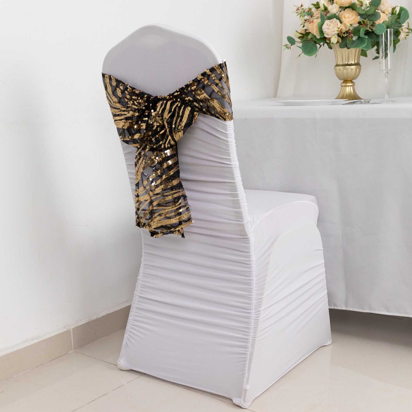 Black and gold wave embroidered sequin chair sash on a white chair.