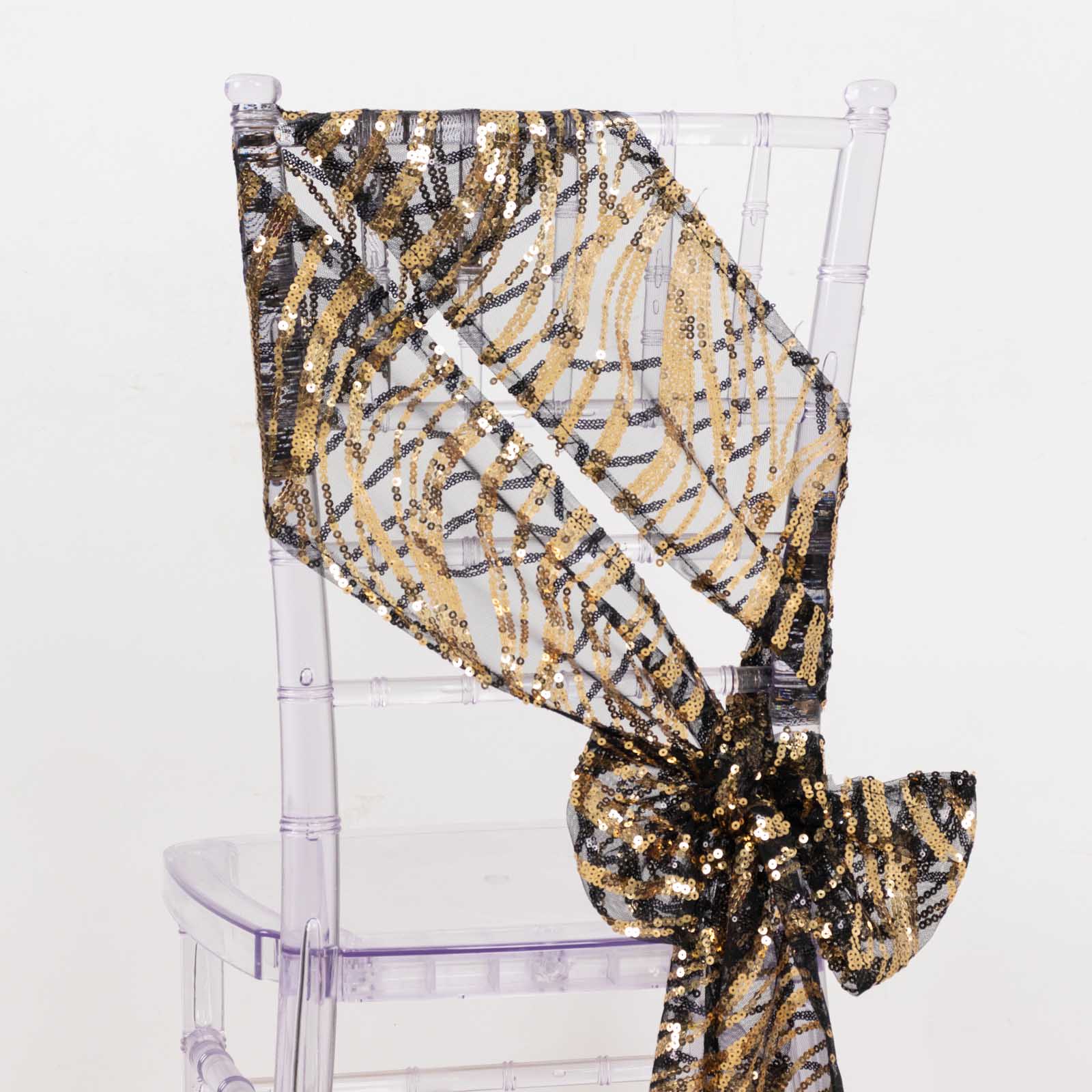 Black and gold wave embroidered sequin chair sash on a clear chair.