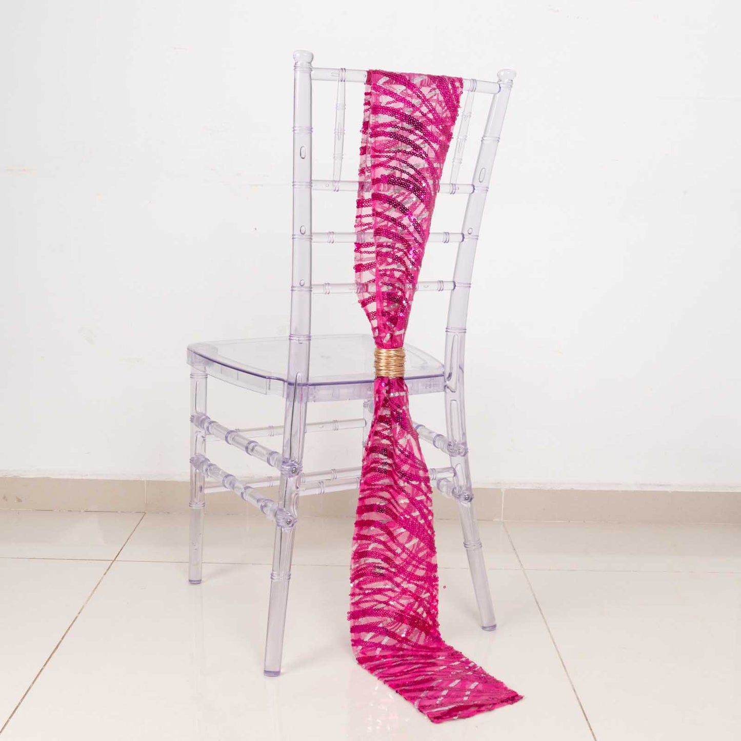 Fuchsia silver wave embroidered sequin mesh chair sash on a transparent chair.