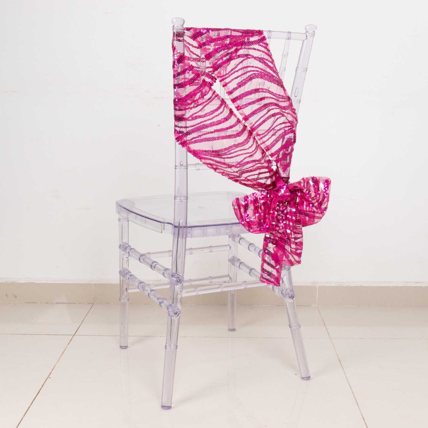 Fuchsia sequin mesh chair sash tied on a transparent chair.