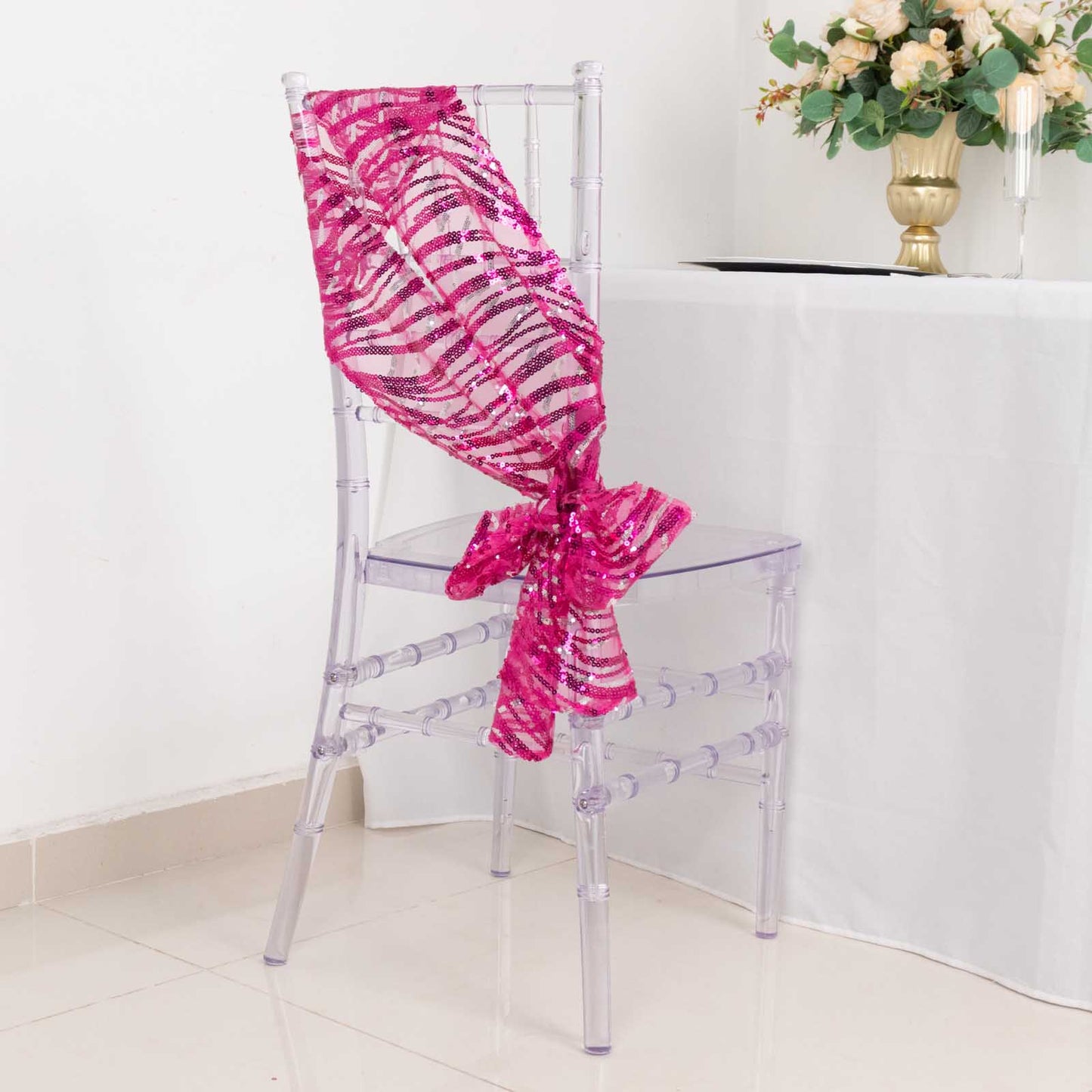 Fuchsia sequin mesh chair sash draped elegantly on a clear chair.