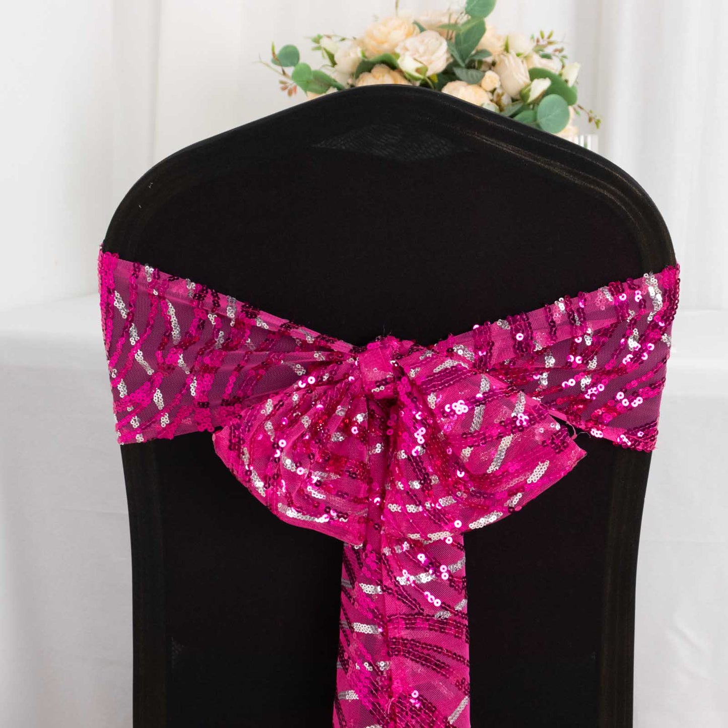 Fuchsia silver wave embroidered sequin mesh chair sash on a black chair.