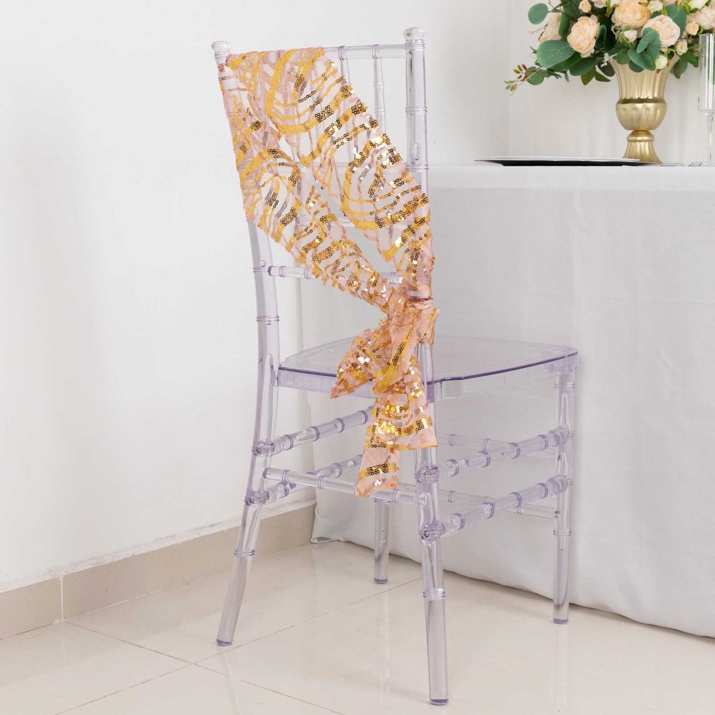 Rose gold mesh chair sash with gold wave sequins draped on a clear chair.