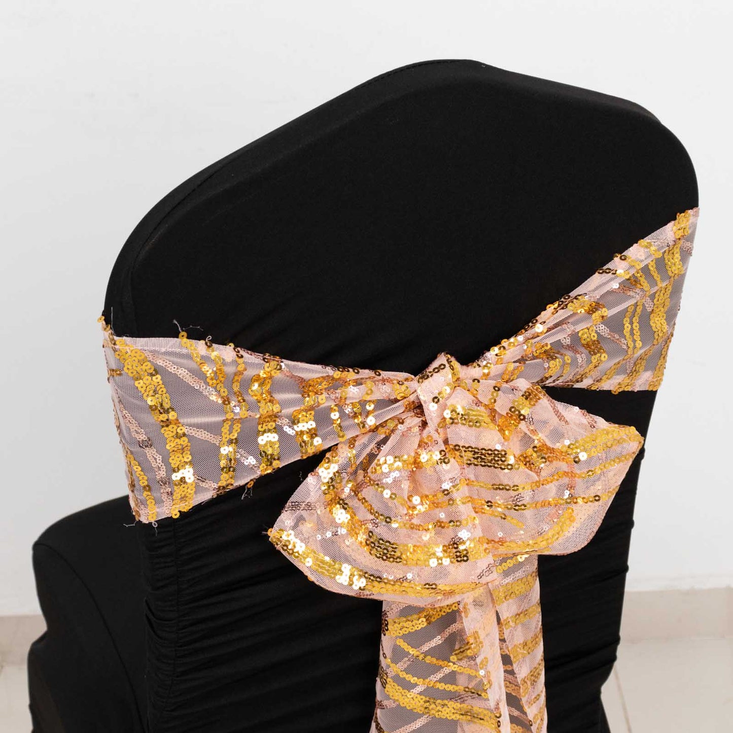 Rose gold mesh chair sash with gold wave embroidered sequins on a black chair.