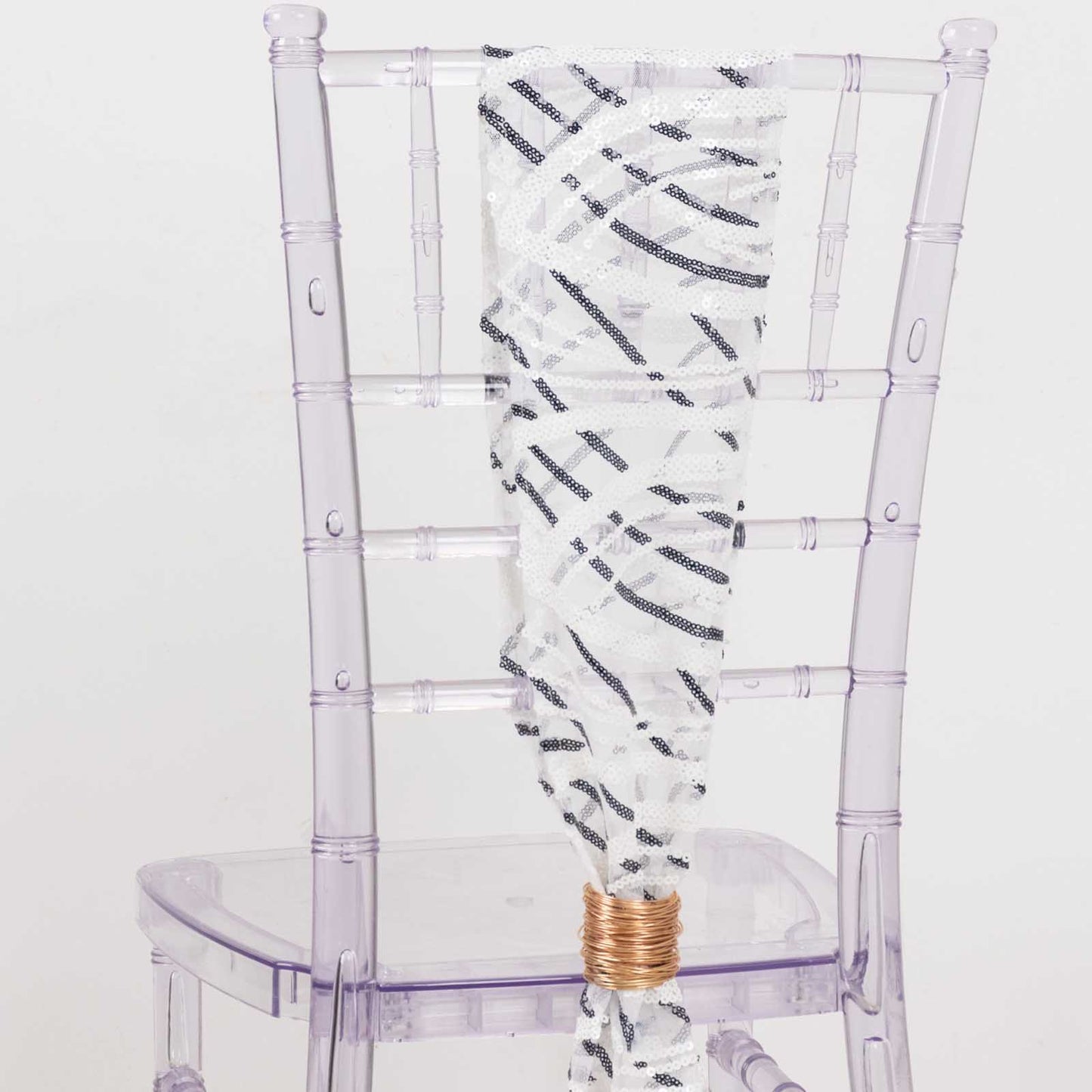 White and black wave embroidered sequin mesh chair sash on a transparent chair.