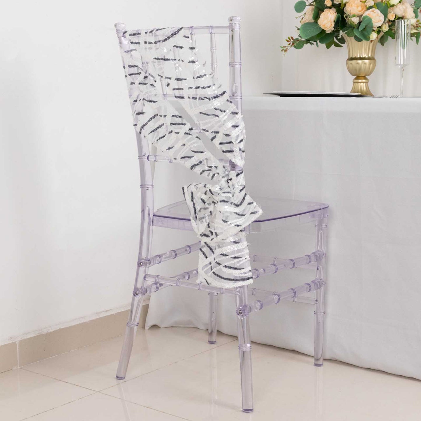 White and black wave embroidered sequin mesh chair sash on a clear chair.