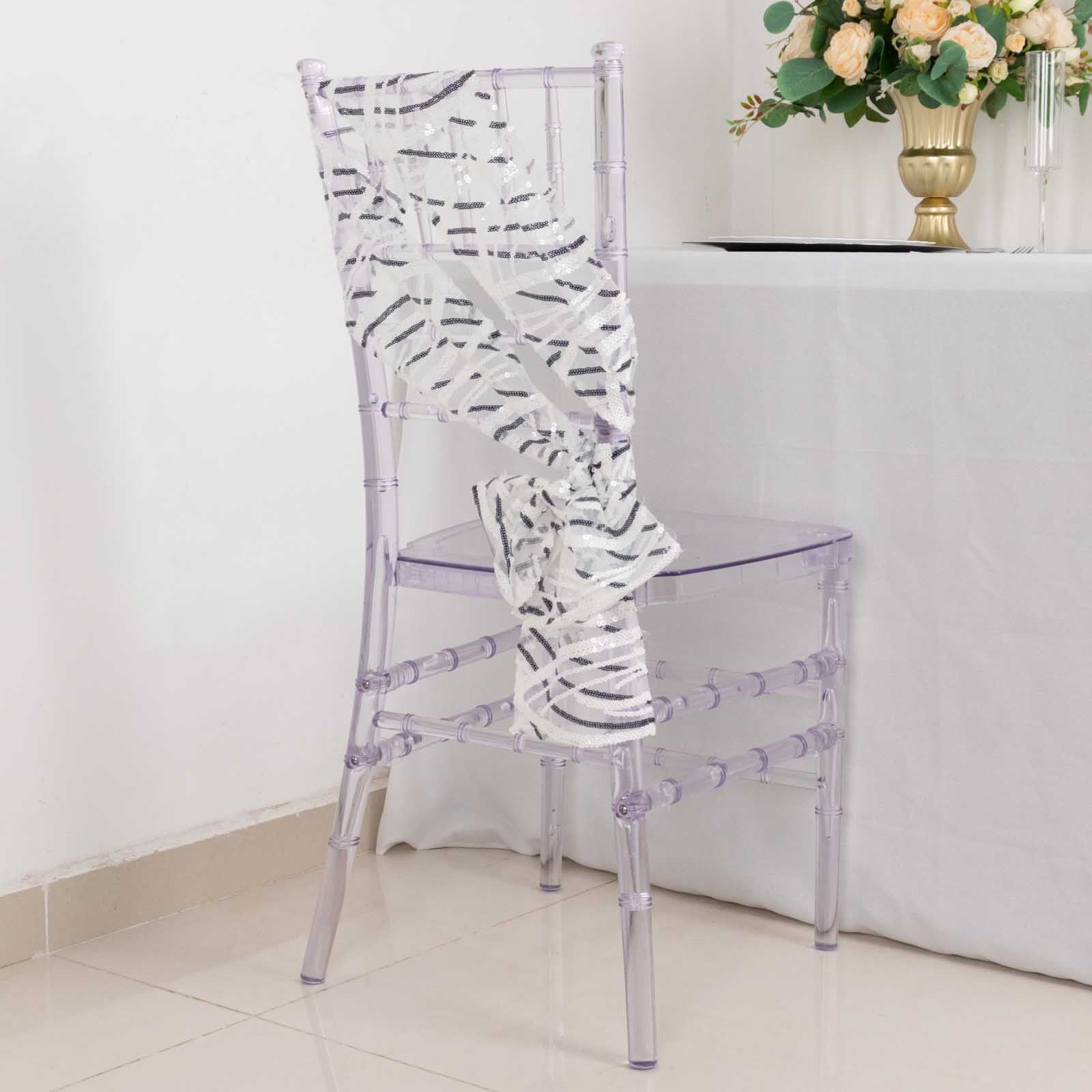 White and black wave embroidered sequin mesh chair sash on a clear chair.