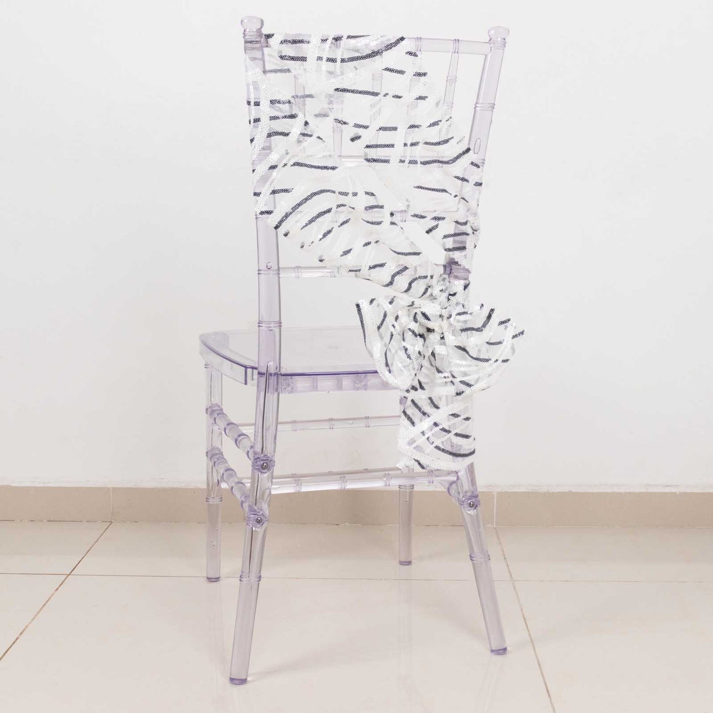 White and black wave embroidered sequin chair sash on a clear chair.