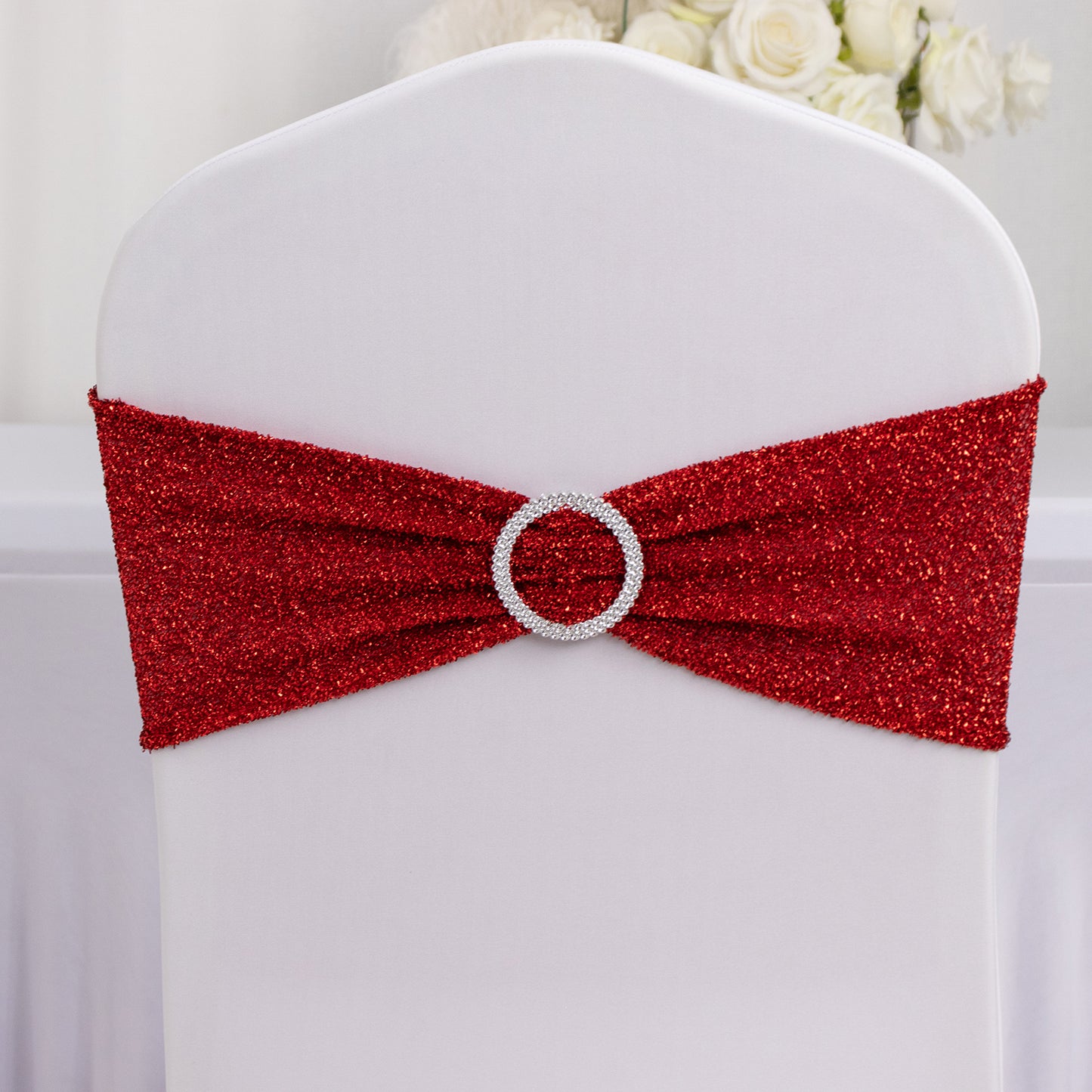 Red shimmer tinsel chair sash with silver rhinestone buckle on white chair.
