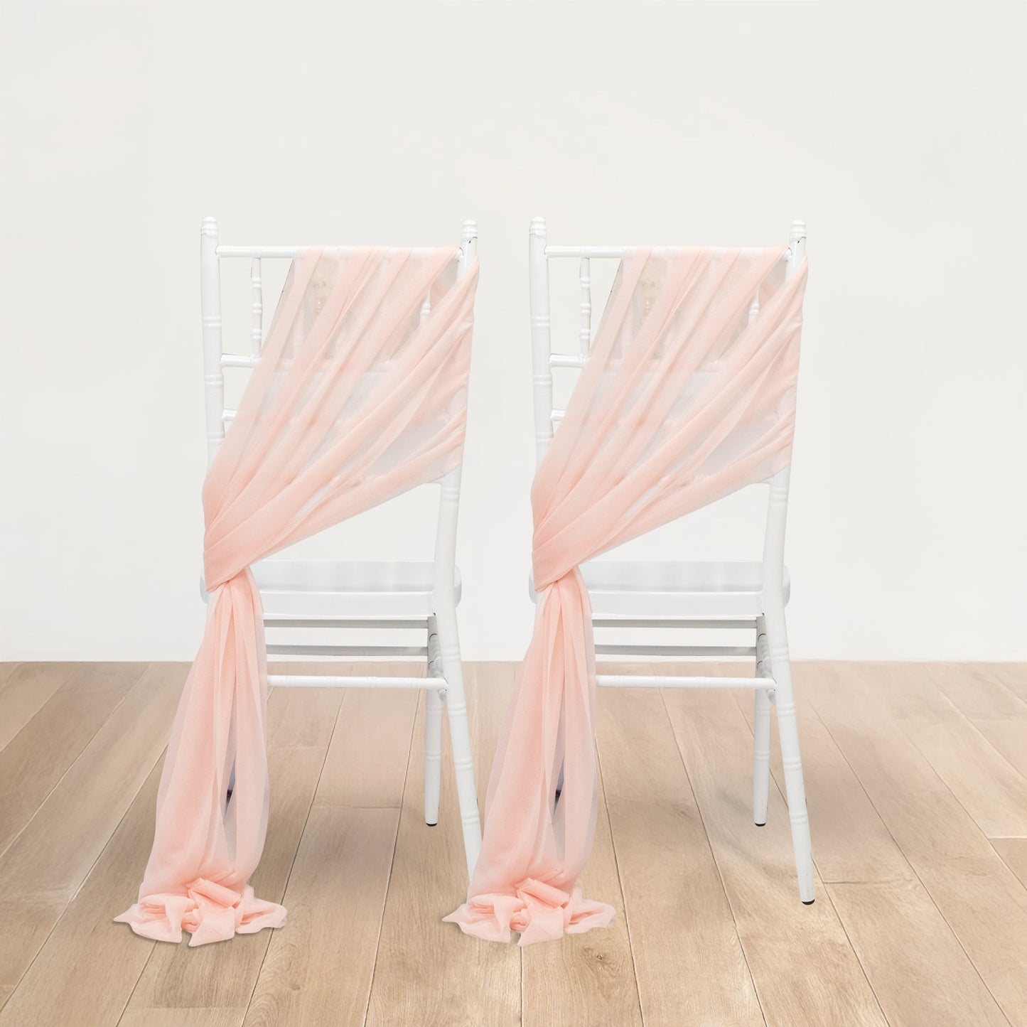 Blush sheer chair drapes elegantly styled on white chairs.