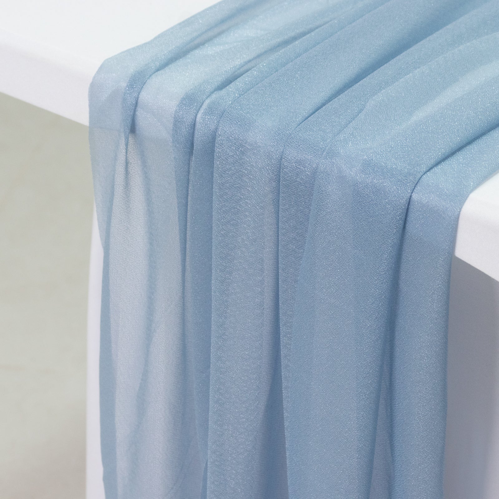 Dusty blue sheer table runner drapes on a white table.