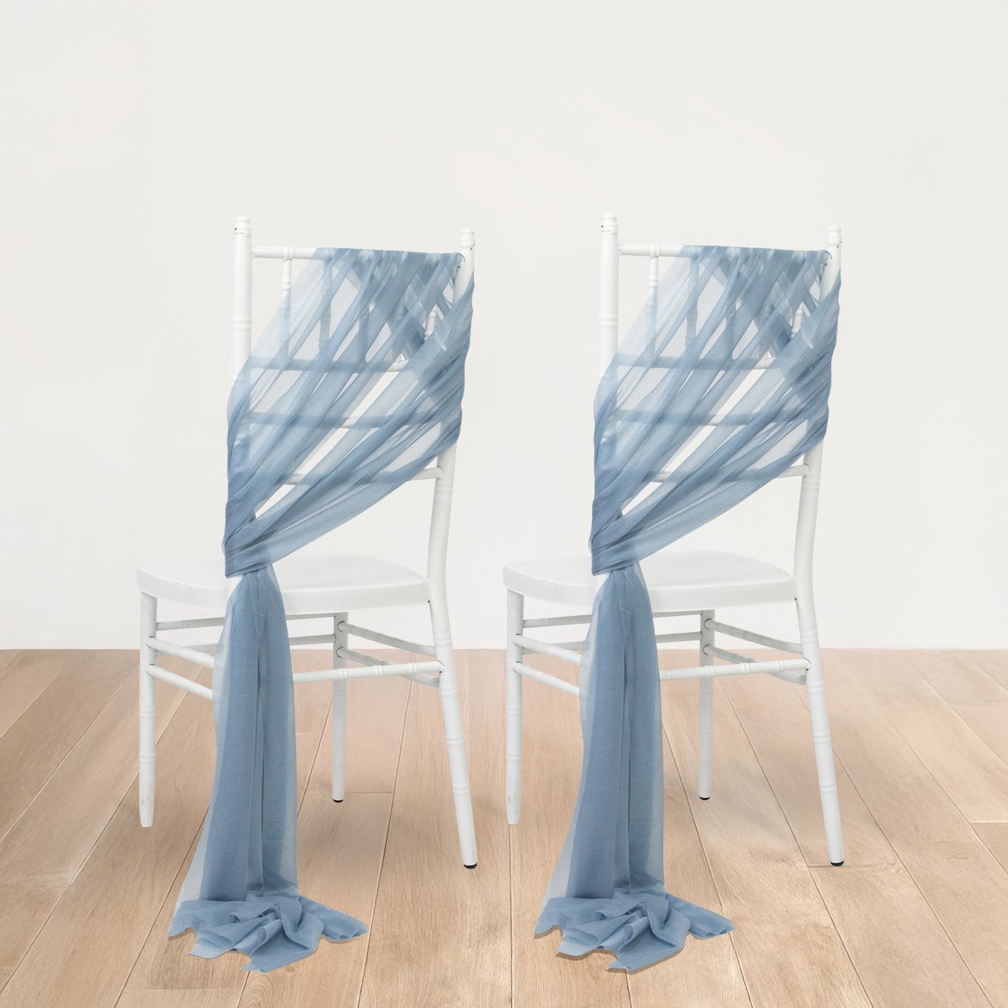 Dusty blue sheer chair drapes elegantly arranged on white chairs.